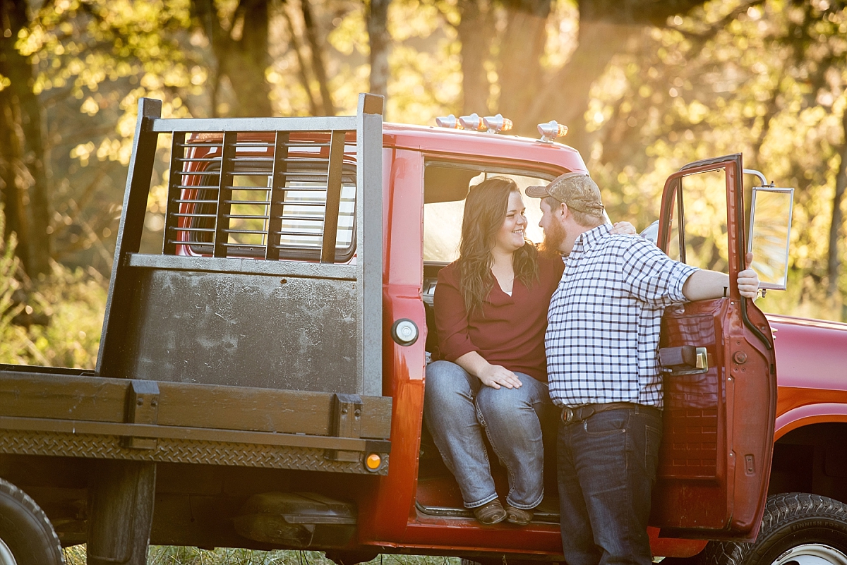 Couple smiling at one another in a vintage red truck during engagement photos