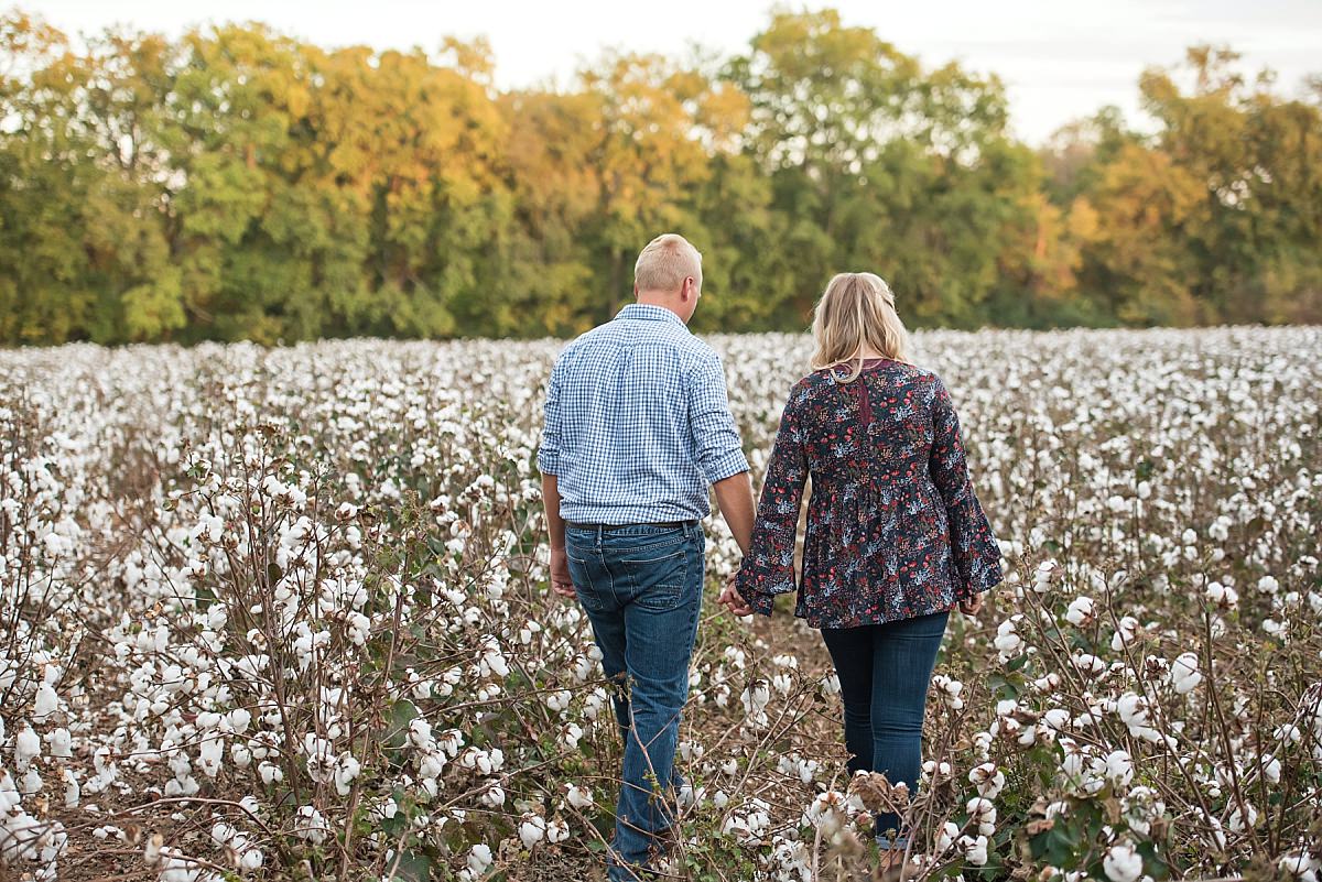 Couple walking through cotton field holding hands during anniversary photos